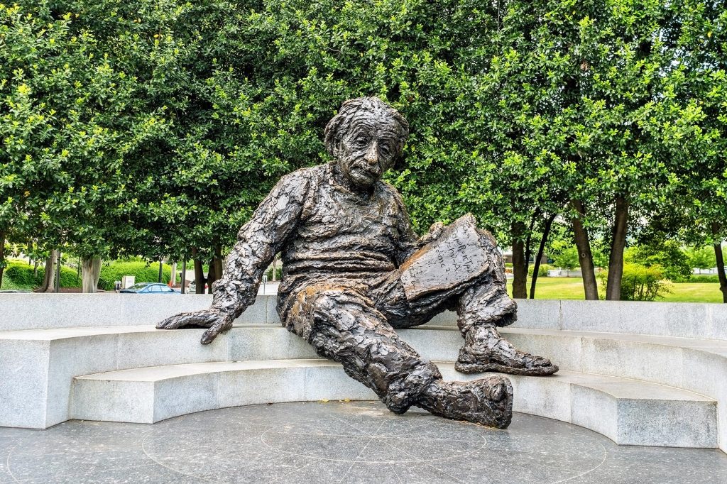 Outdoor scientist sculpture holding a book on stone steps in a park