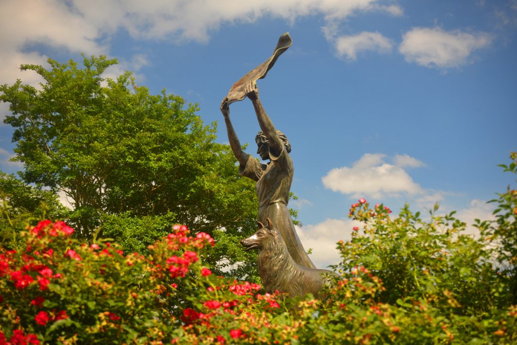 Woman raising fabric with dog statue in a Savannah garden